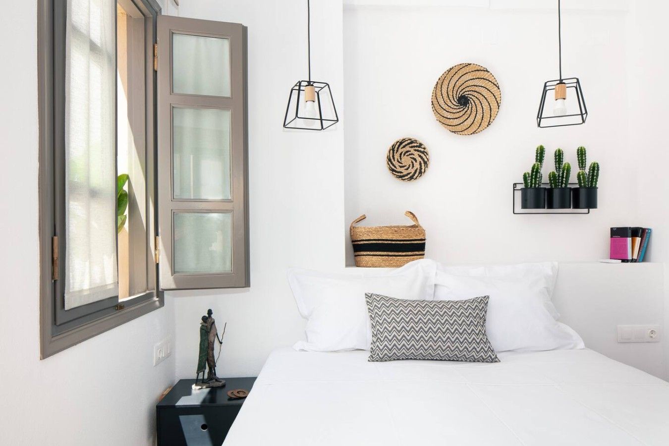 A bedroom with a bed, a nightstand, a wall-mounted shelf with books and a plant, and a window with curtains.
