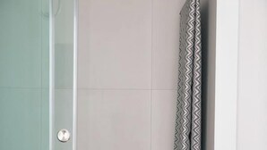 Un baño con cabina de ducha de vidrio, un perchero con una toalla estampada y una botella en el suelo.
