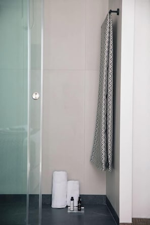 A bathroom with a glass shower enclosure, a towel rack with a patterned towel, and a bottle on the floor. - Gateway Suites - Pathos (Ρέθυμνο)