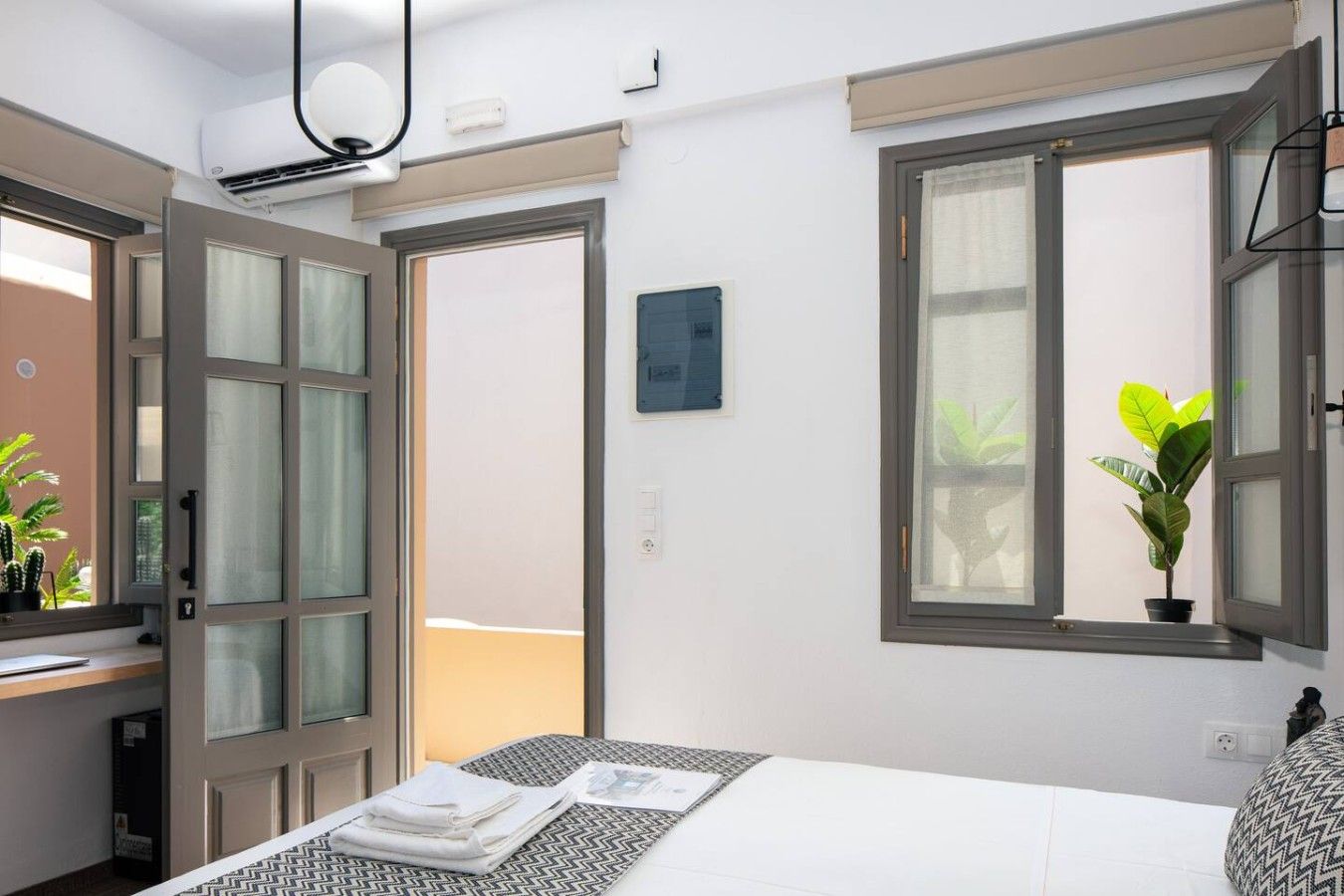 Habitación de hotel con cama, escritorio, ventana con planta y puerta que da a otra habitación.