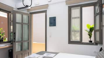 Habitación de hotel con cama, escritorio, ventana con planta y puerta que da a otra habitación.
