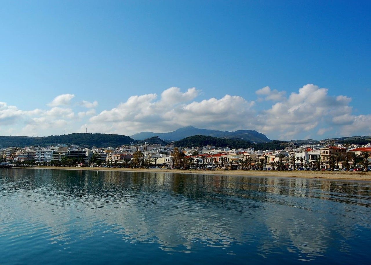 Un paisaje urbano costero con edificios a lo largo del malecón, cielo despejado y montañas al fondo.