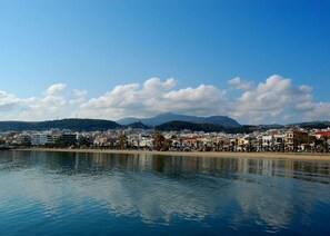 Un paisaje urbano costero con edificios a lo largo del malecón, cielo despejado y montañas al fondo.