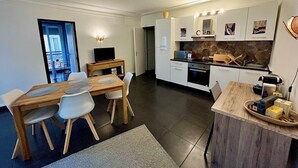 A modern kitchen with white cabinets, a dining area with a wooden table and chairs, and a small island with a sink. - Superb modern T3, 5 minutes from the Old Port (Marseille)