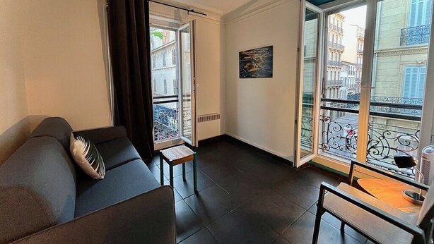A living room with a sofa, a small table, and a view of a cityscape through a balcony. - Superb modern T3, 5 minutes from the Old Port (Marseille)