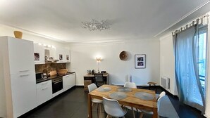 A modern kitchen with white cabinetry, a wooden dining table with four chairs, and a built-in oven. - Superb modern T3, 5 minutes from the Old Port (Marseille)