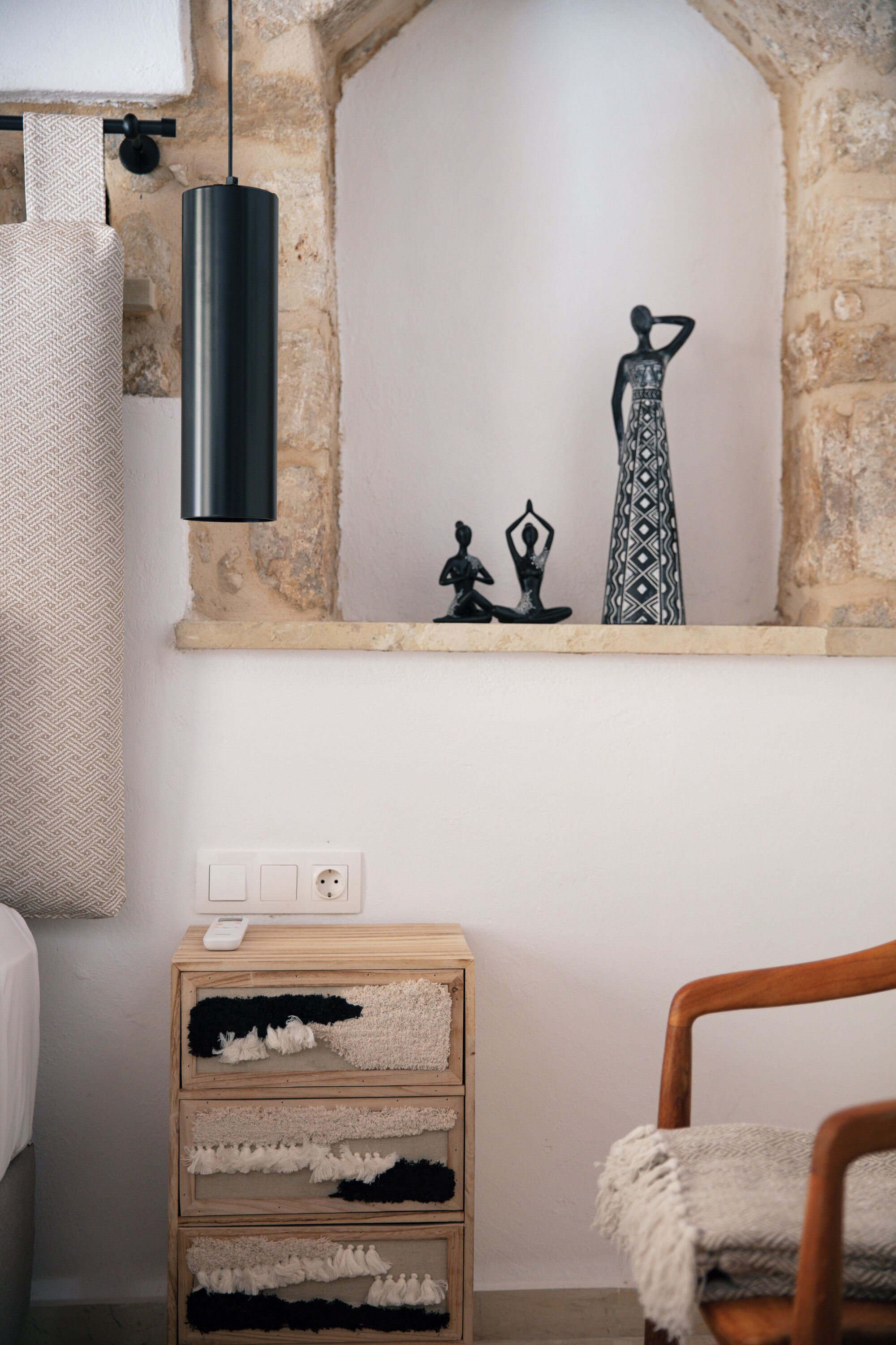 Una habitación con pared de piedra, un aparador de madera, una lámpara colgante y una silla de madera.