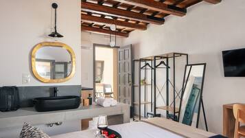A hotel room with a large bed, a round mirror, a black sink, and a television on the wall.