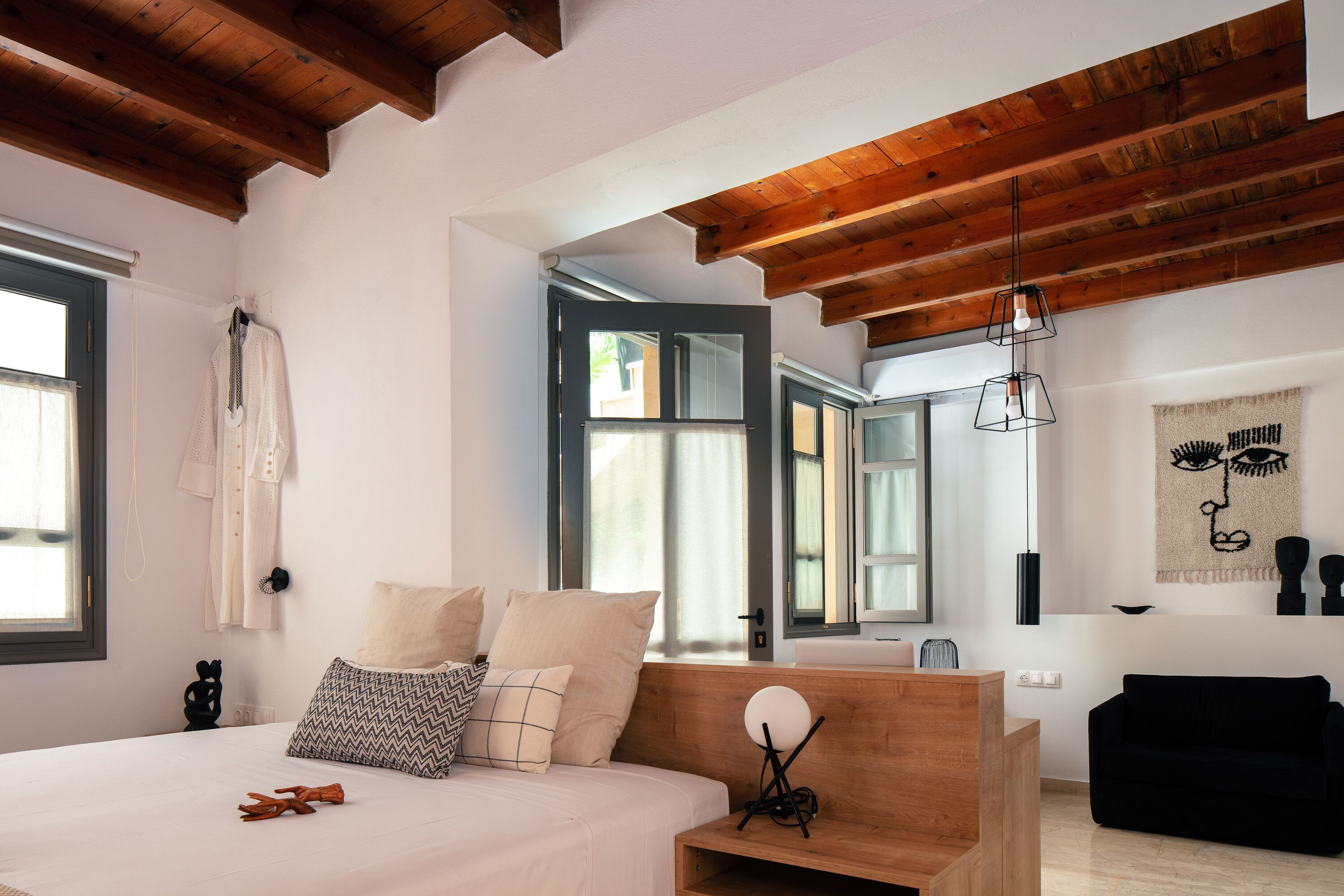 A bedroom with a wooden headboard, a bed with multiple pillows, a bedside table with a lamp, and a black sofa in the corner.