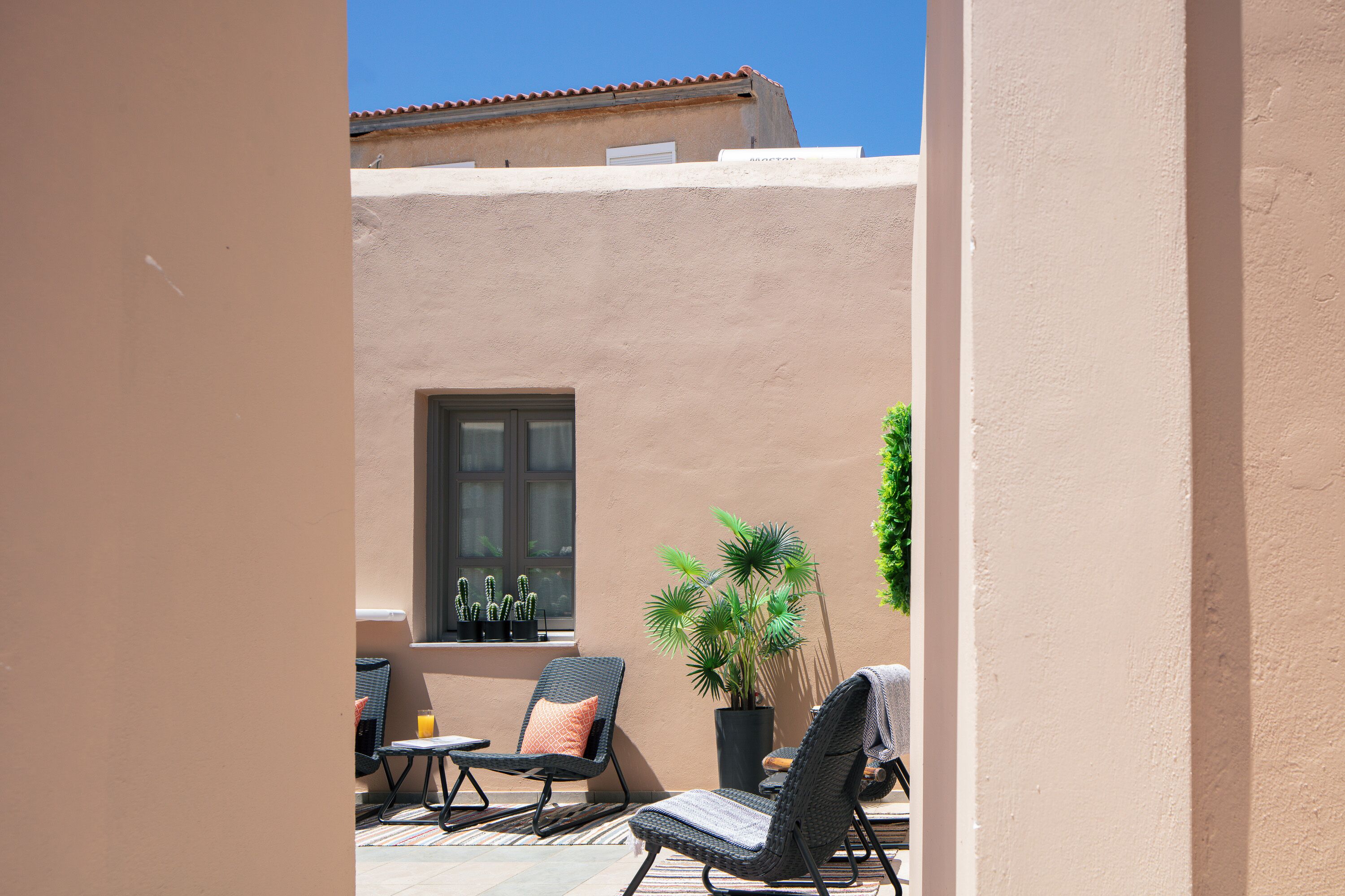 A patio with two wicker chairs, a table, and a potted plant.