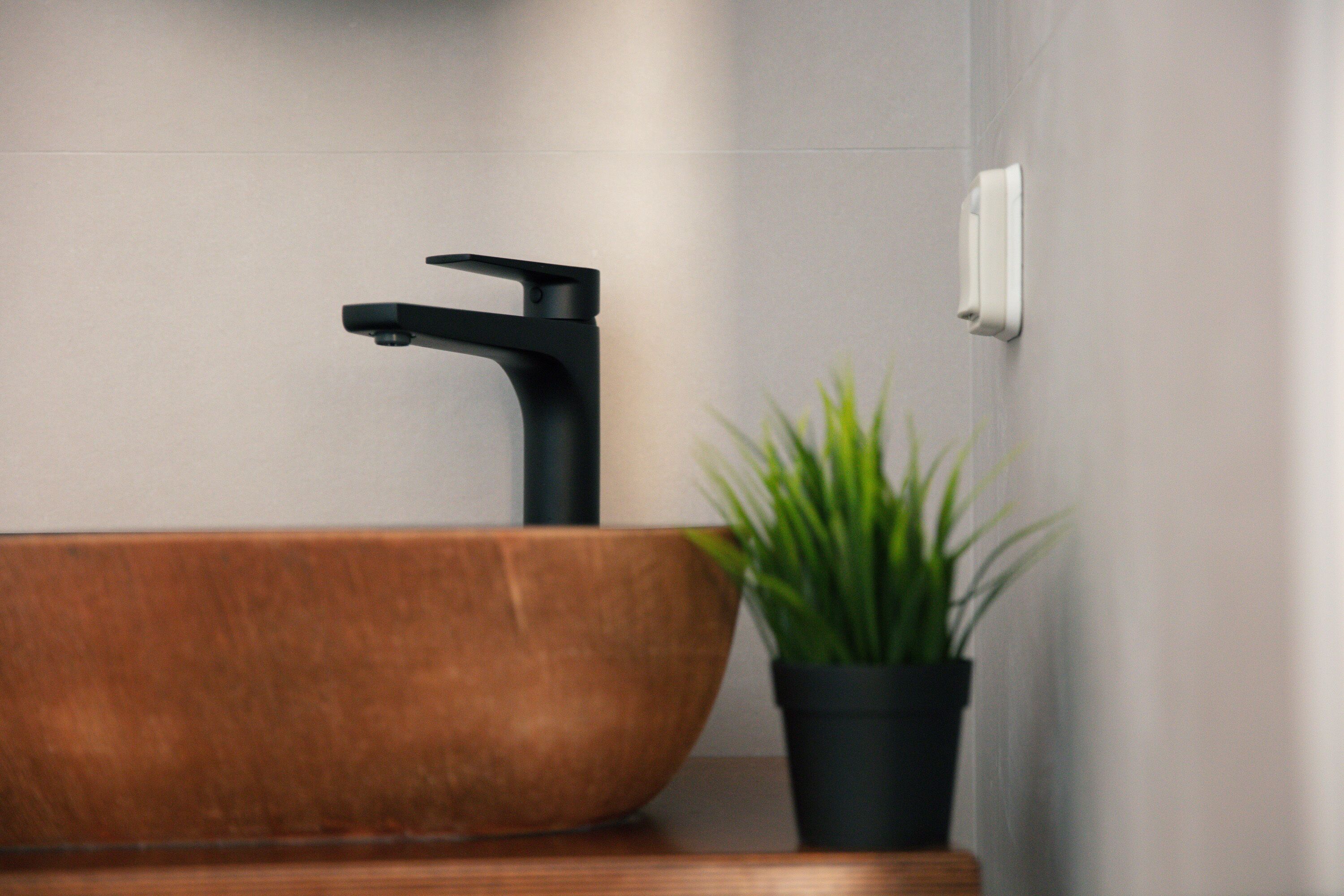 A modern bathroom with a wooden basin, a black faucet, and a potted plant.