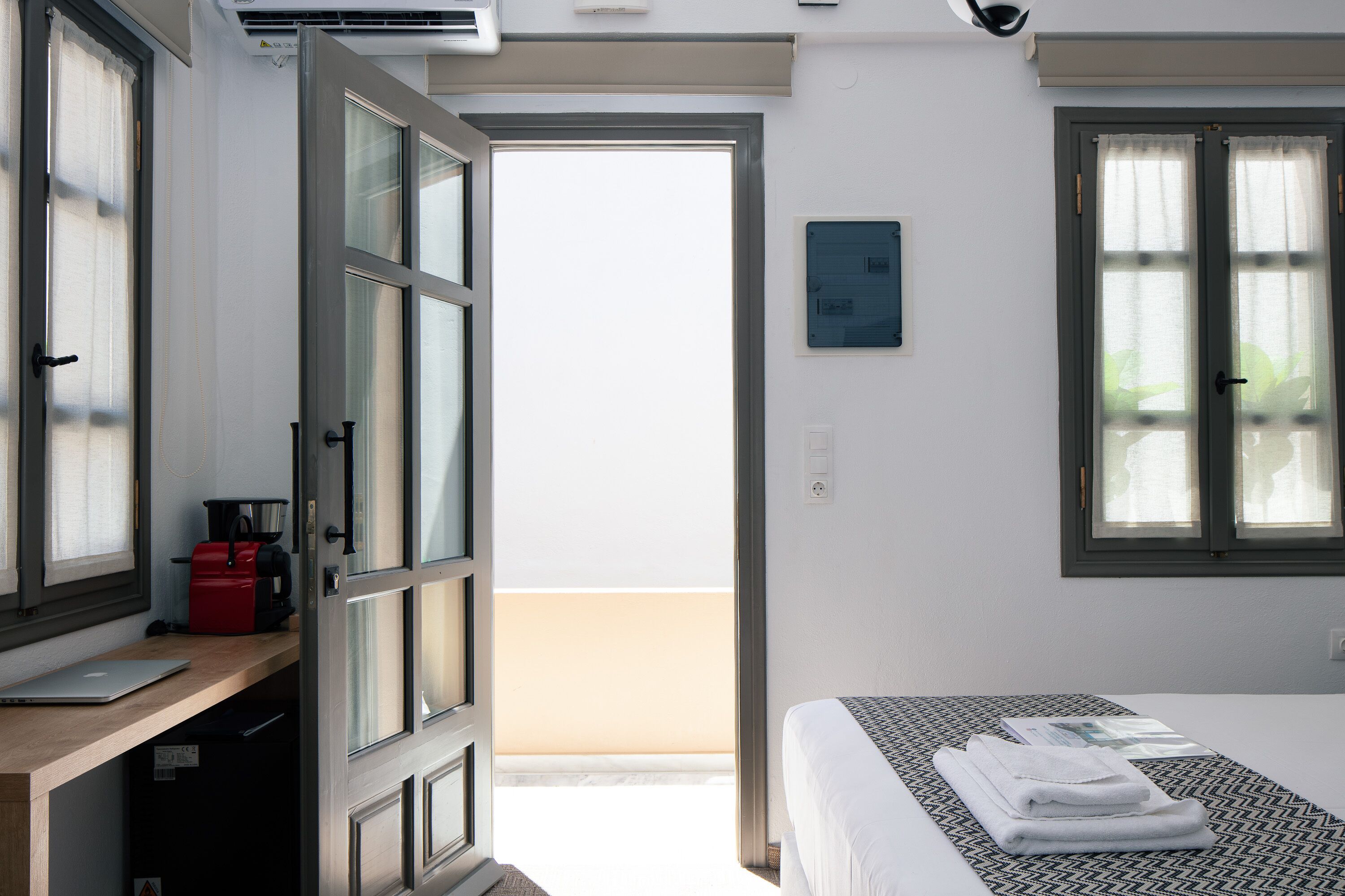 Une chambre d’hôtel avec un lit, un bureau avec un ordinateur portable, un sac rouge et une vue sur l’extérieur.