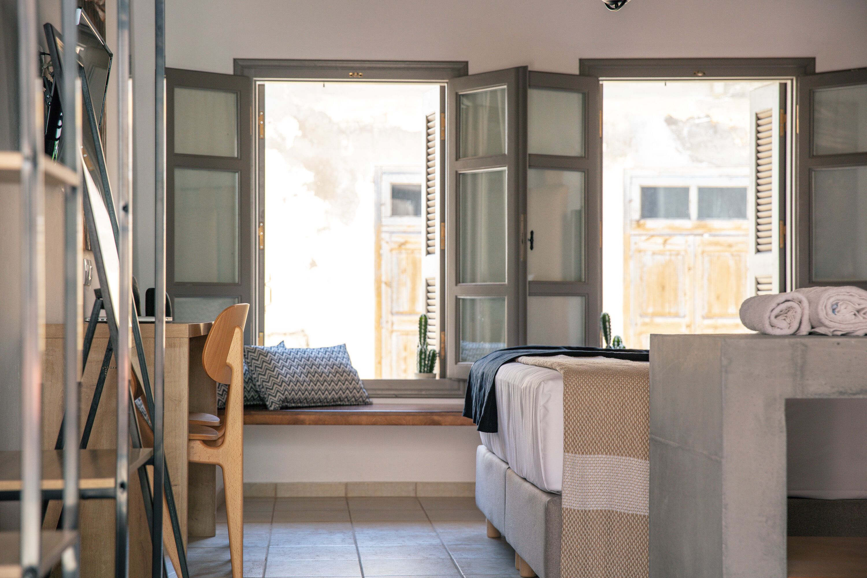 Una habitación con cama, ventana, silla y una pequeña mesa.