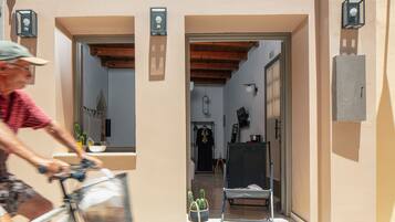 Un callejón estrecho con un ciclista pasando, que conduce a un edificio con techo de madera y una puerta.