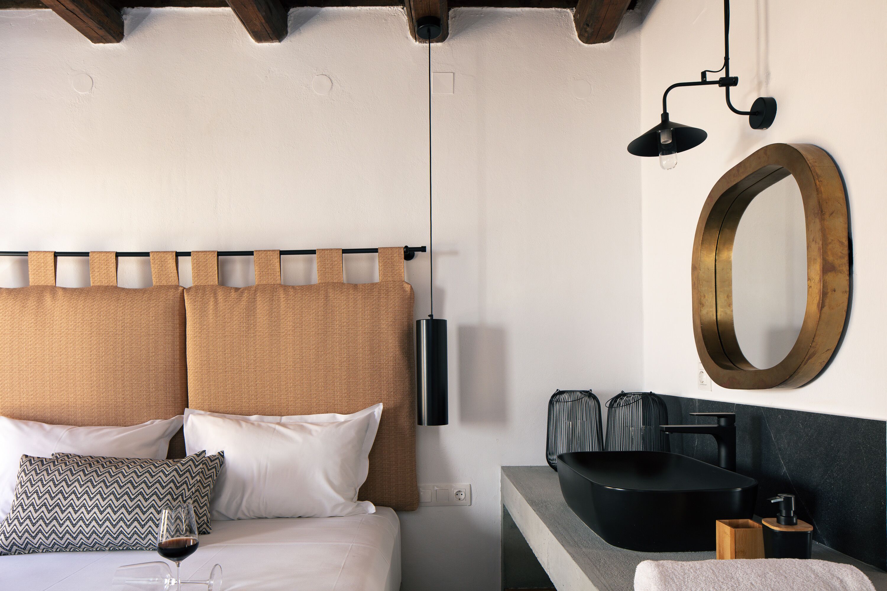 Una habitación de hotel moderna con una cama, almohadas, una mesita de noche con un lavabo negro, un espejo y una lámpara colgante.