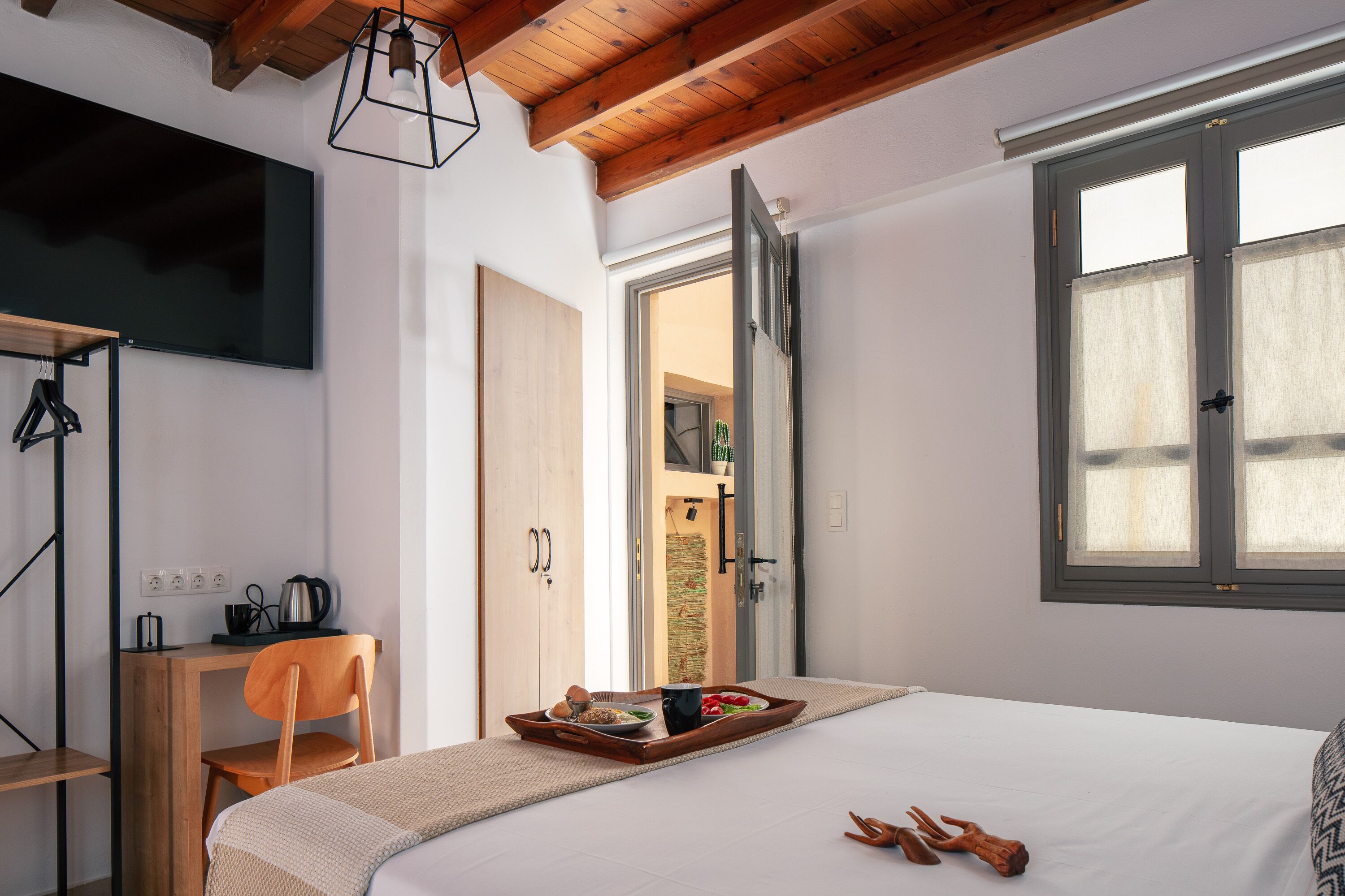 Une chambre à coucher avec un lit, un bureau et une chaise. On y trouve un plateau avec de la nourriture et une tasse posés sur le lit.