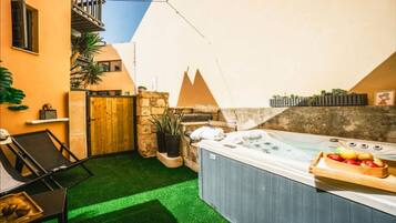 A spa area with a hot tub, artificial grass, a wooden gate, and potted plants.