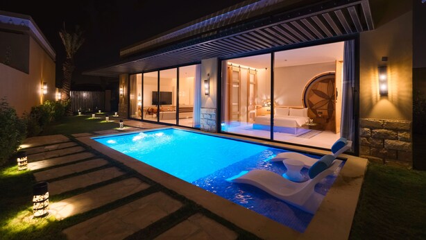 Een modern buitenzwembad met een afgesloten spa-gedeelte van glas, stenen trappen en sfeerverlichting.