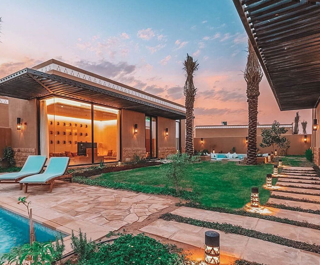 Ein modernes Haus mit Pool, Liegestühlen und einer gut beleuchteten Terrassenfläche.