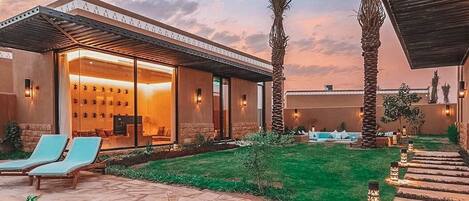 Een modern huis met een zwembad, lounge stoelen en een goed verlicht terras.