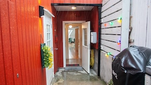 A narrow corridor with a red wall on one side and a white wall on the other, leading to a door. There is a potted plant on the red wall and a barbecue grill on the white wall. - Harbour View - Marina - City Centre (Tórshavn)