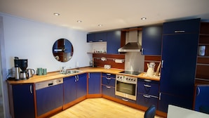 A modern kitchen with blue cabinets, a wooden countertop, a built-in oven, and a round mirror on the wall. - Harbour View - Marina - City Centre (Tórshavn)
