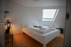 Een wit bed in een kamer met dakraam, houten vloer en een kamerplant.