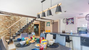 A modern kitchen with a dining area, featuring a staircase, a kitchen island, and various kitchen appliances. - Modern duplex loft in the heart of Annecy's old town for 10 people (annecy)