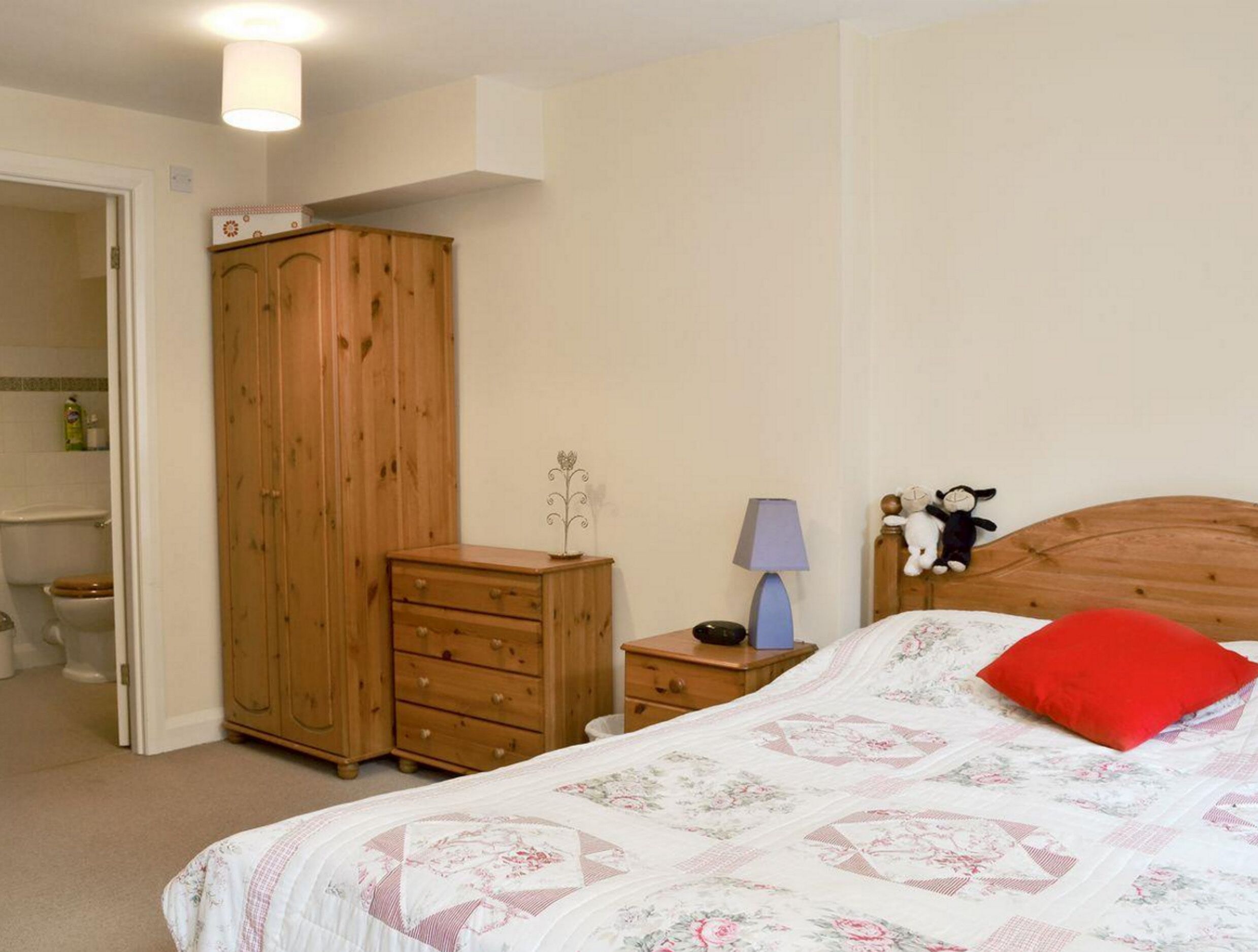 A bedroom with a bed, a wooden wardrobe, a nightstand, and a lamp.