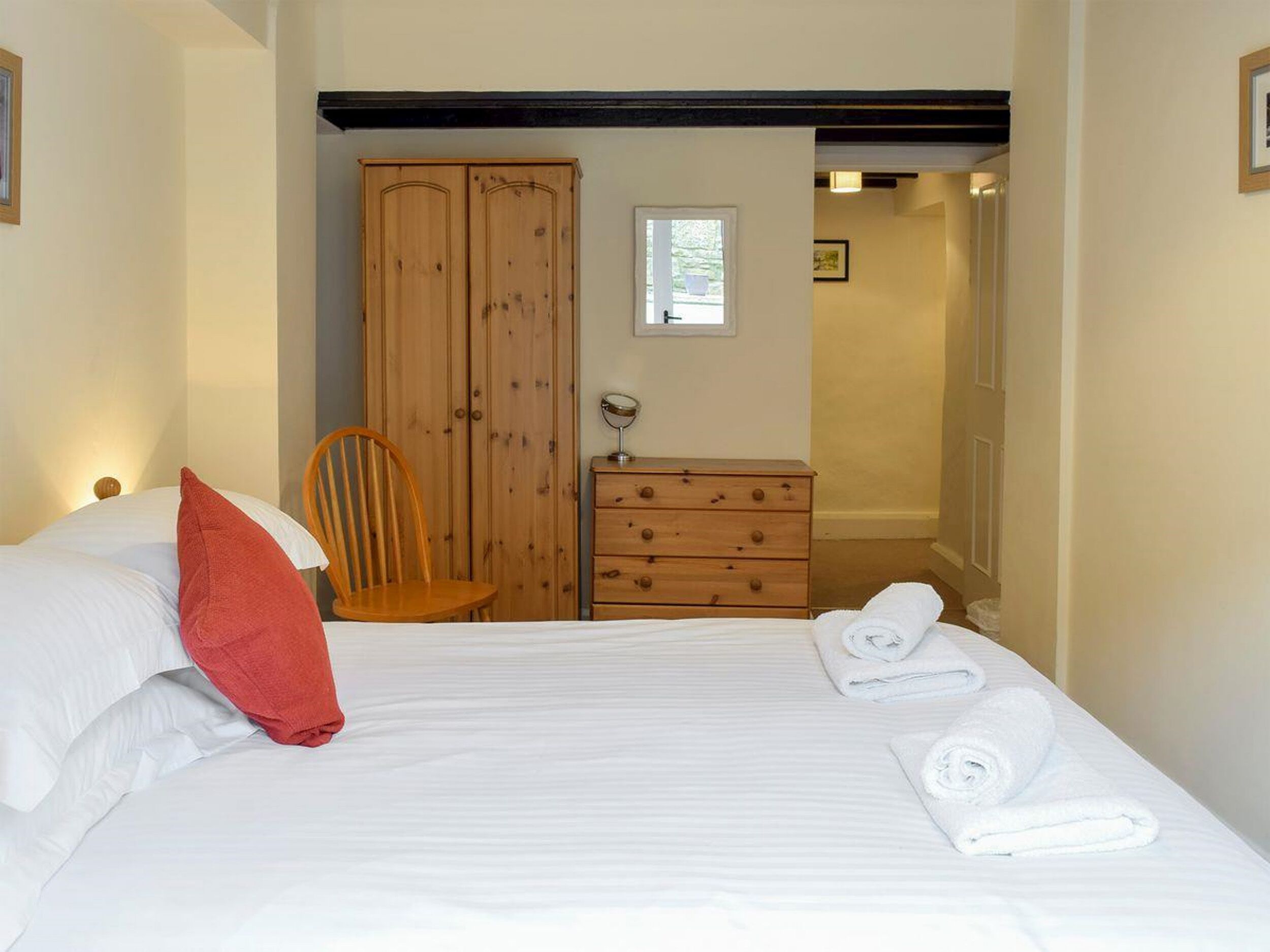 Ein Schlafzimmer mit einem Bett, einem Holzschrank, einem Stuhl, einer Kommode und einem kleinen Fenster.