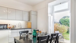 Una cocina moderna con armarios blancos, una mesa de comedor con sillas negras y vistas al jardín a través de un amplio ventanal.