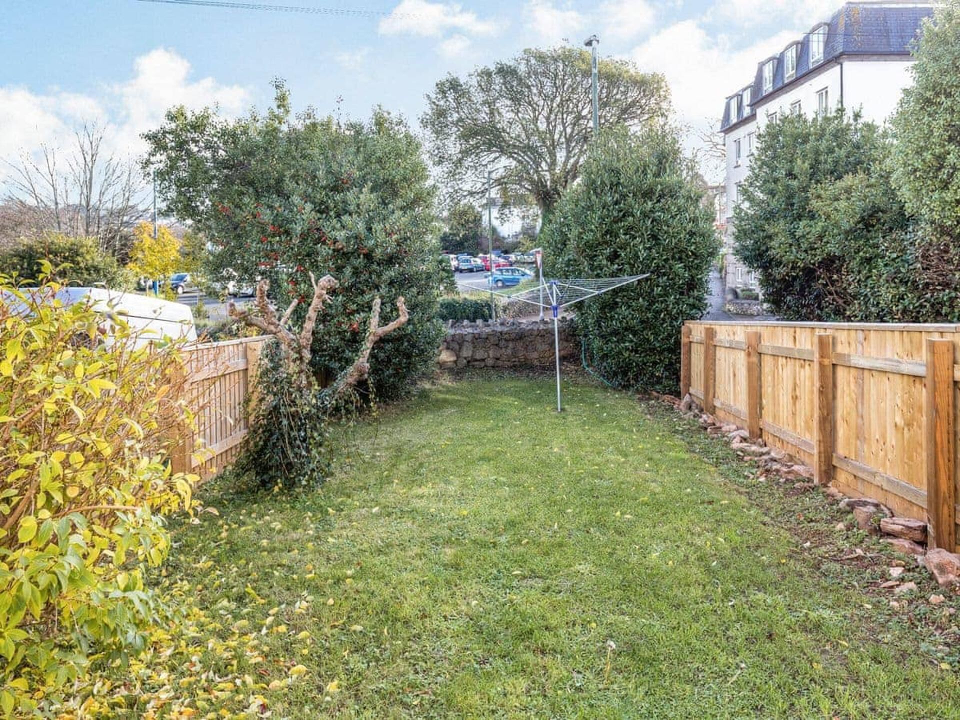 A backyard with a wooden fence, a clothesline, and various trees and shrubs.