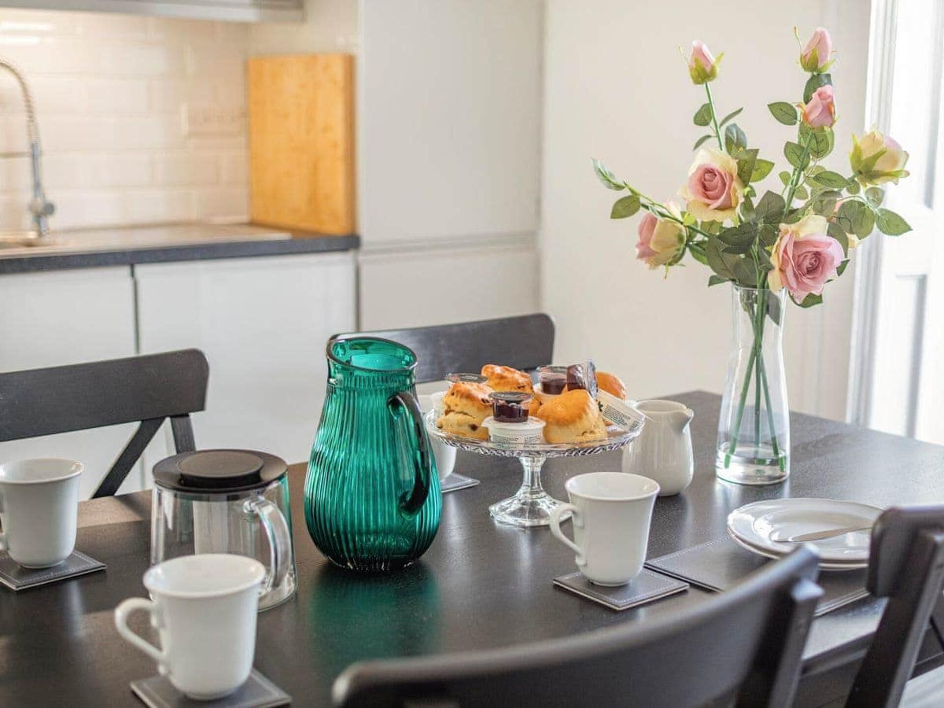 A breakfast setting with a coffee pot, pastries, and a vase of flowers on a table.