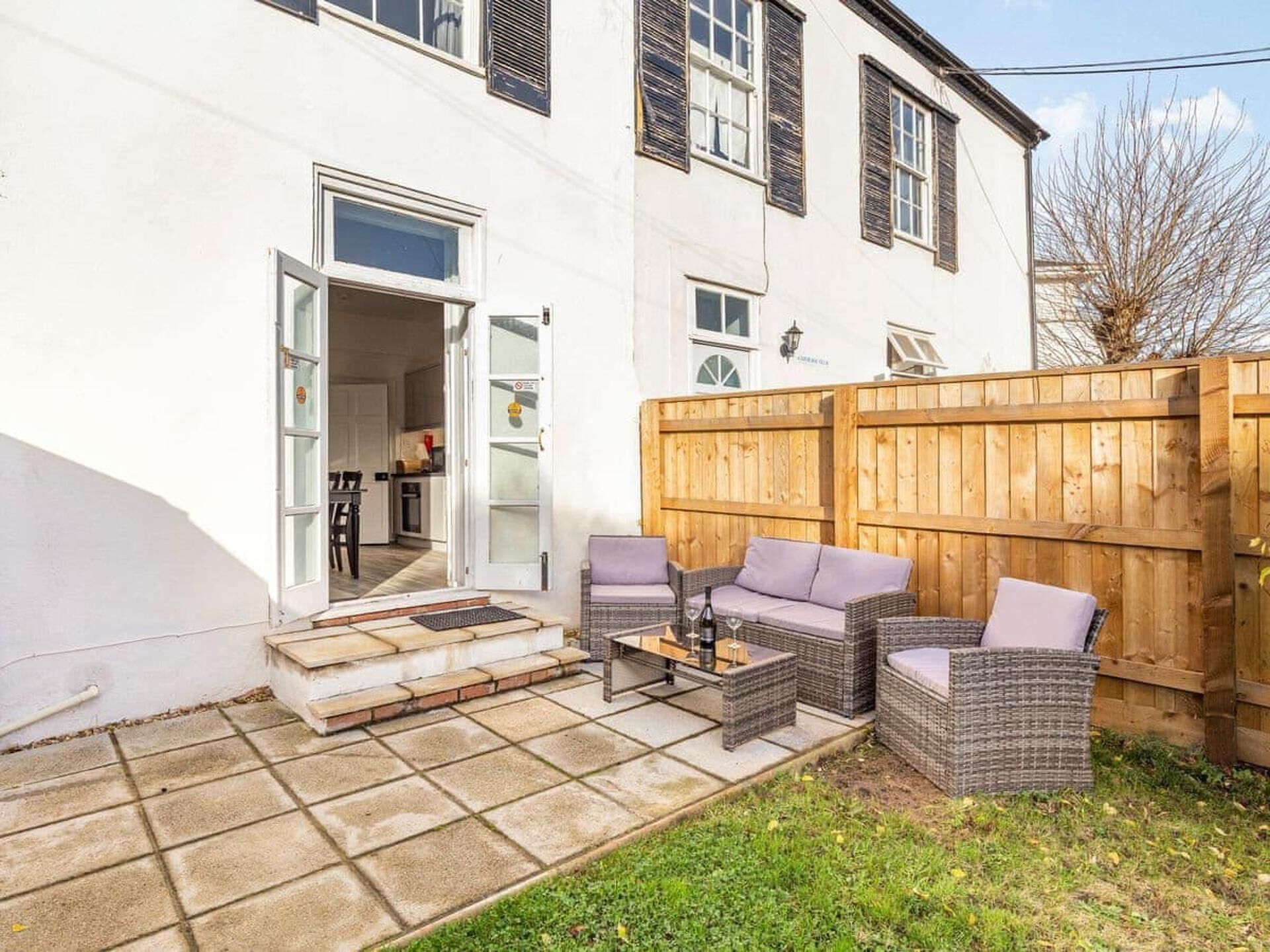 A white building with a wooden fence, a patio with wicker furniture, and a visible kitchen area.