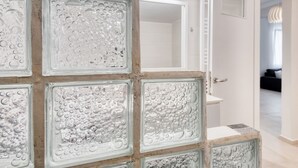 Een badkamer met een glazen blokkenwand, een witte wastafel en een deur naar een gang.