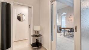 Een hal met een spiegel, een tafel met een lamp, en een deur naar een eetgedeelte met stoelen en een tafel.