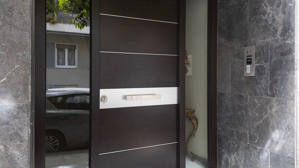 Een moderne deur met horizontale lijnen en een handgreep, in een gebouw met marmeren wanden en een zichtbare lift.
