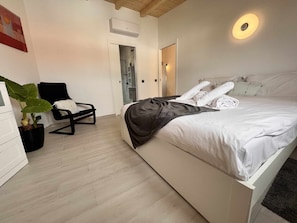 A modern bedroom with a bed, a chair, a potted plant, and a shower area. - "Casa Bella" Apartment with SPA, Pool & Sauna (Poço Partido)