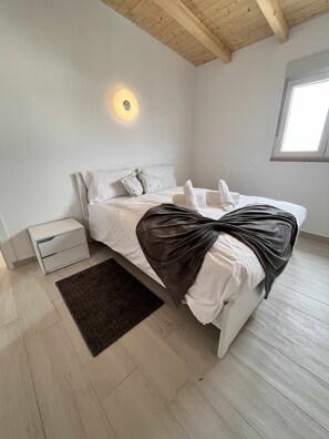 Un dormitorio con cama, mesita de noche, ventana y lámpara de techo.