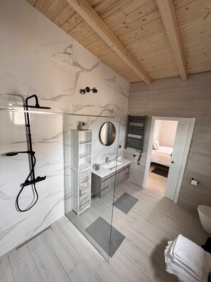 Un baño moderno con ducha de vidrio, tocador con espejo y techo de madera.