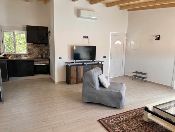 Una sala de estar moderna con un sillón gris, una mesa de centro de vidrio y un televisor sobre un mueble de madera.