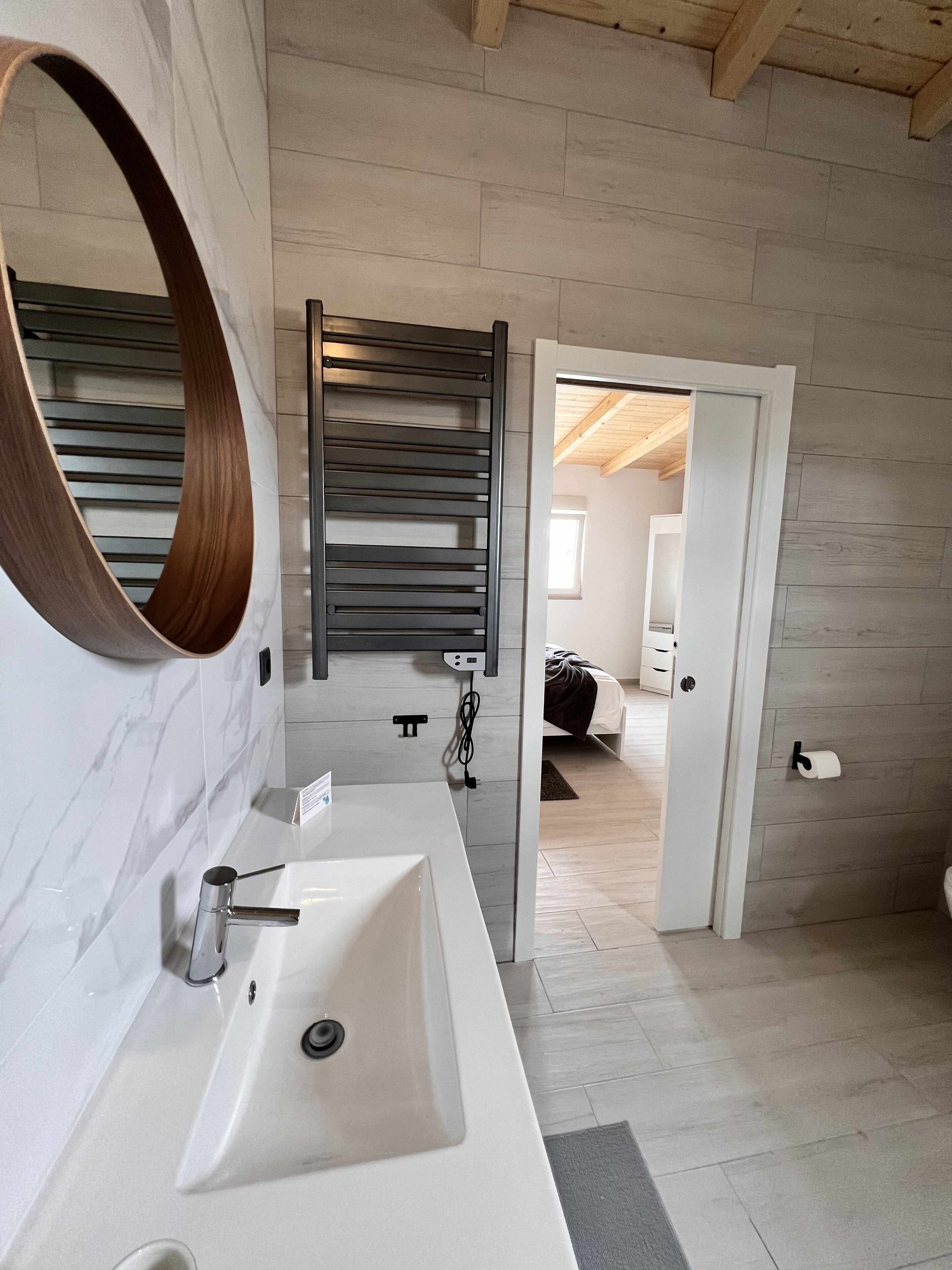 A modern bathroom with a white sink, a large mirror, and a wooden slatted shower enclosure.