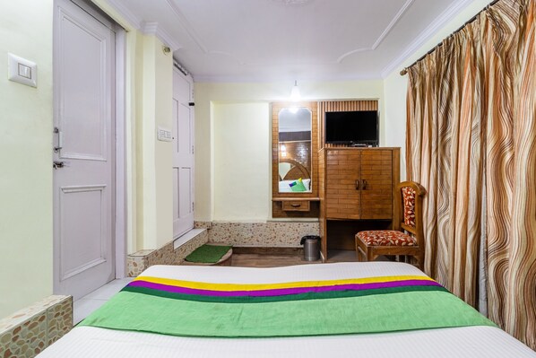 A hotel room with a bed, a chair, a small table, a mirror, a TV, and a curtain.