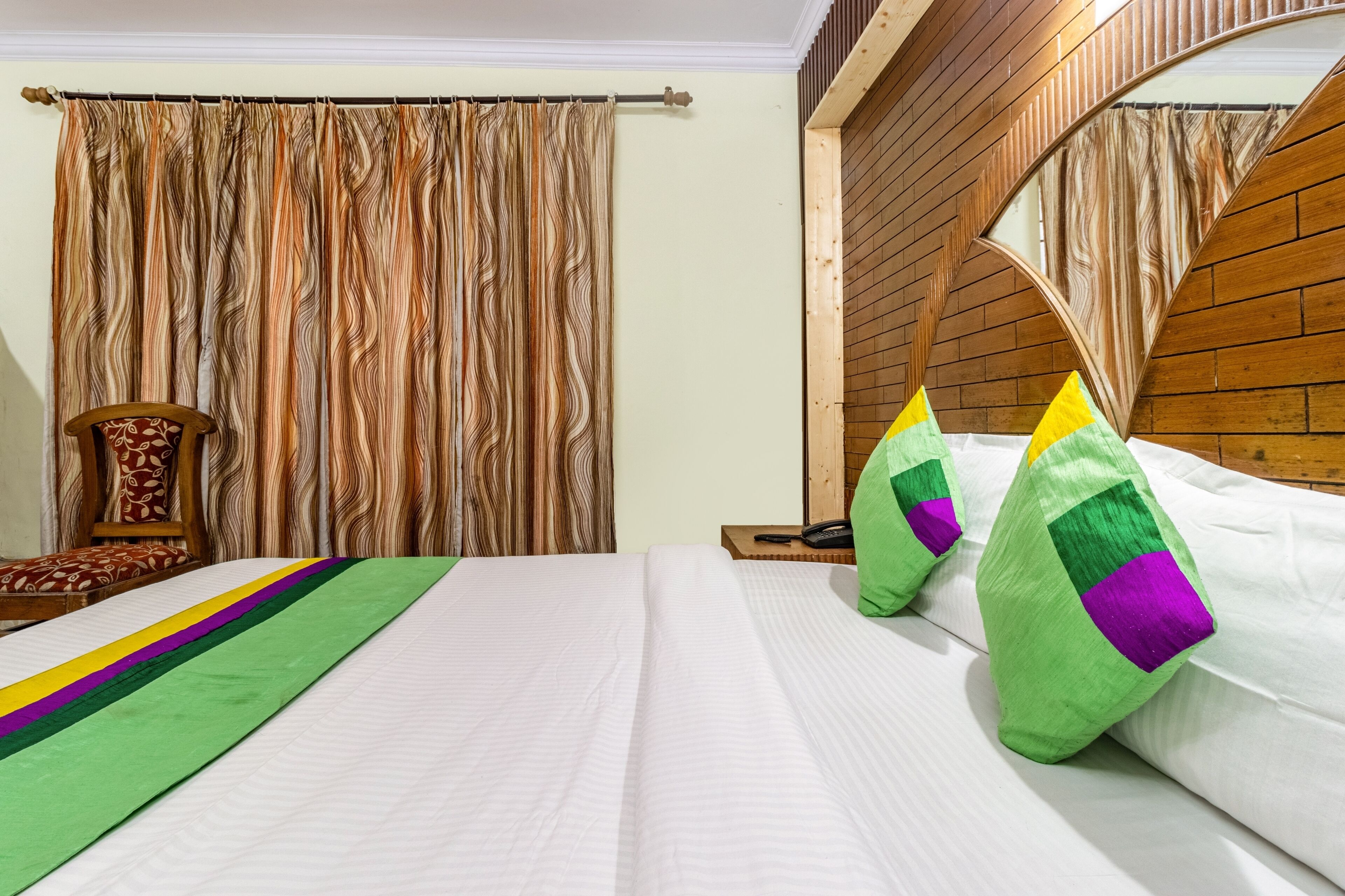 A hotel room with a bed, a wooden headboard, a chair, and a curtain.