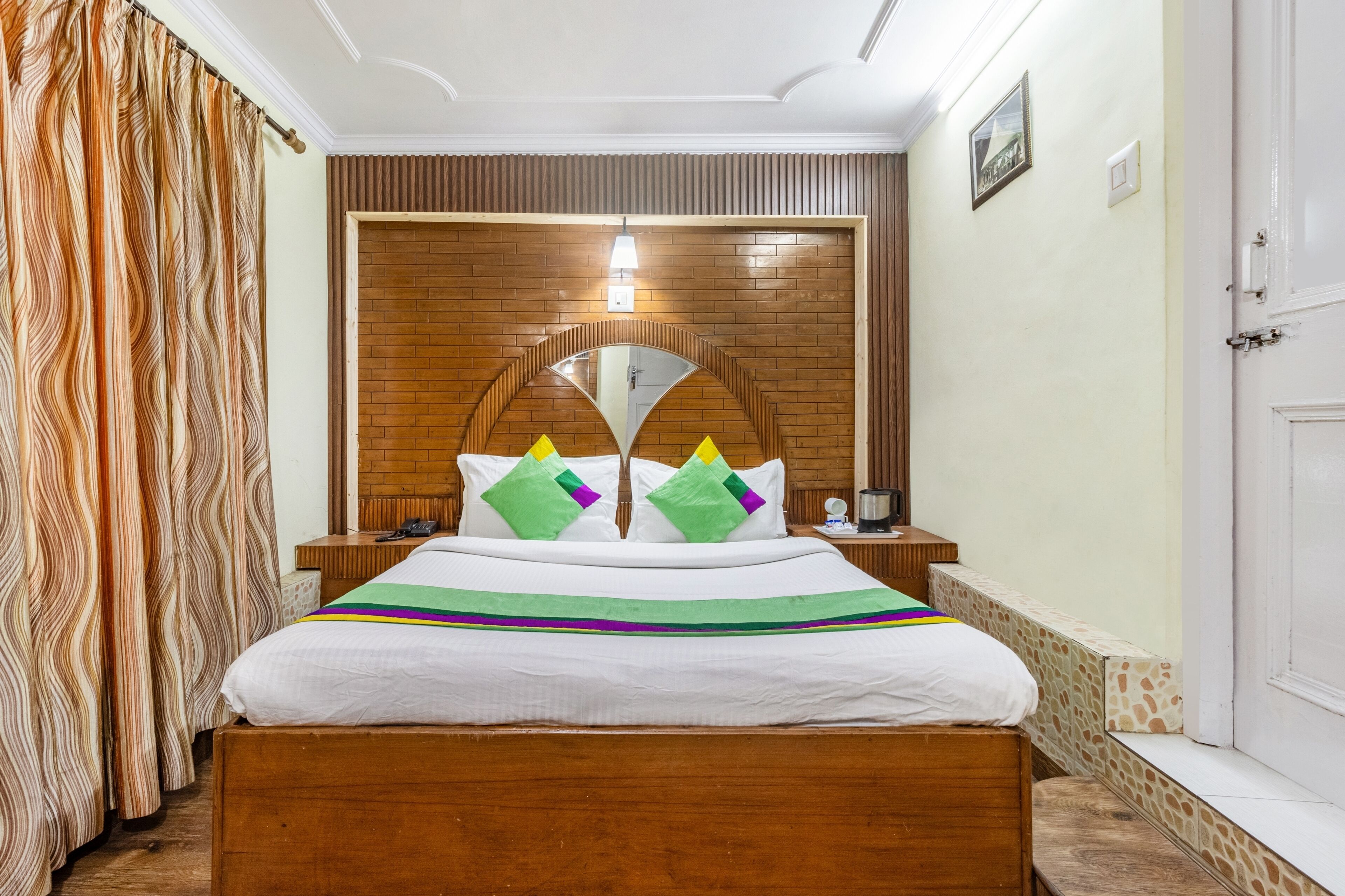 A hotel room with a wooden bed, a brick-patterned headboard, and a small bedside table with a lamp.