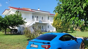 A blue sports car parked in front of a white house with a red roof, surrounded by greenery.