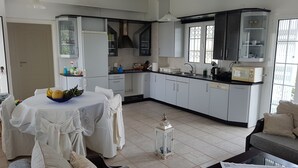 A modern kitchen with white cabinets, a dining area with a table set for two, and a large window providing natural light.