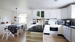 A modern kitchen with white cabinets, a black countertop, and a dining area with a table and chairs. - Liljulon - Views - Location (Ljosa)