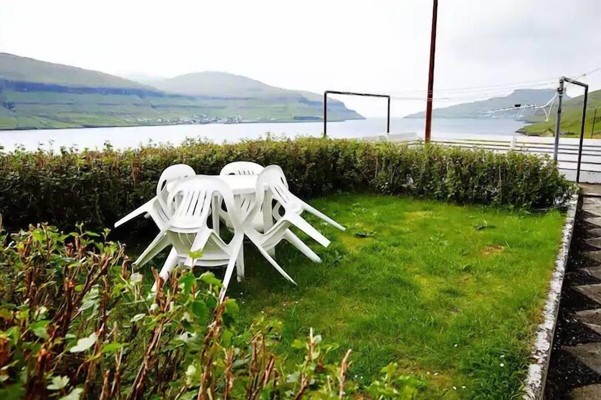 A grassy area with white plastic chairs and a view of a body of water and hills in the background.