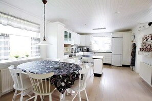 A modern kitchen with white cabinetry, a dining area with a patterned tablecloth, and a hanging light fixture.